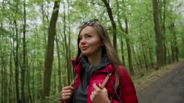 Retrato de mulher bonita turista em jaqueta vermelha com mochila andando na floresta espessa primavera no dia ensolarado. Recreação, bela vista, esportes, viagens — Vídeo de Stock