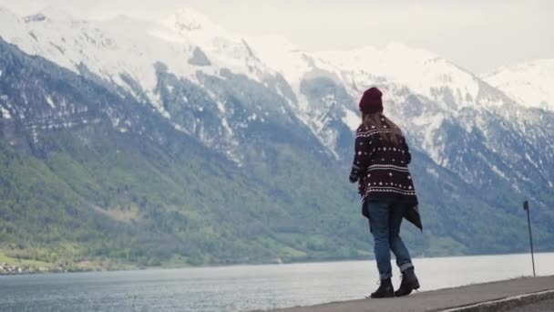 Mujer con abrigo estampado y sombrero de punto alimenta a los pájaros con pan junto al lago — Vídeos de Stock