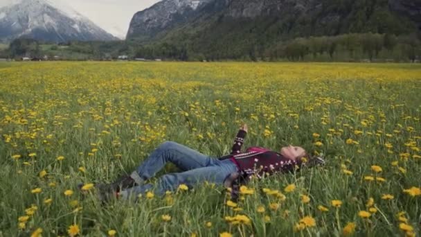 Молодая красивая женщина отдыхает в поле с цветами одуванчика. Вид сбоку — стоковое видео
