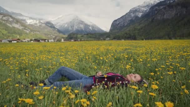 Young beautiful woman is relaxing in flower field against the background of the Swiss Alps — Stockvideo