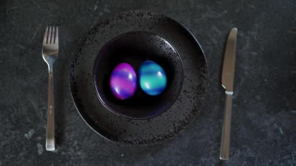 Vista superior de dos coloridos huevos de Pascua en un plato negro sobre un fondo oscuro — Vídeo de stock