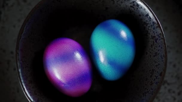 Horní pohled na dvě barevná velikonoční vajíčka na černém talíři. Zavřít