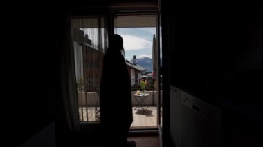 Ekose sarılı genç kadın oturma odasından doğal dağ manzaralı terasa çıkıyor. Arka görüş