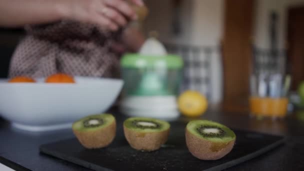 Mädchen nimmt Kiwi vom Tisch, um Saft zu pressen. verschwommen — Stockvideo