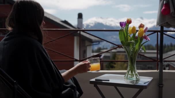 Giovane donna beve succo sul balcone, montagne di neve sullo sfondo. Vacanza e relax. Bella ragazza godere della vista sulle Alpi svizzere al mattino. Da vicino. — Video Stock