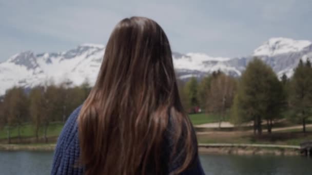 Mujer morena de pelo largo de pie y con vistas panorámicas del lago de montaña en Suiza. Vista trasera. Foco flotante Primer plano — Vídeos de Stock