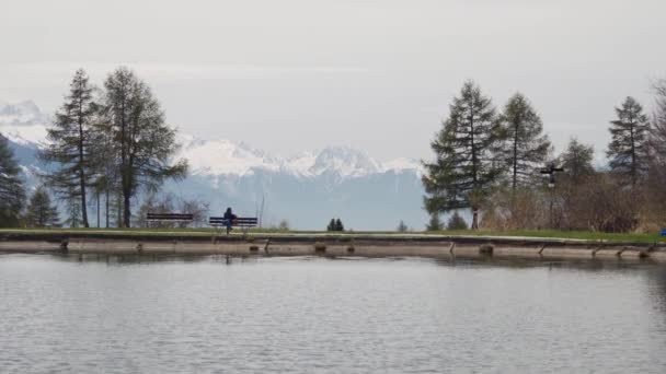 Turistická dívka sedí na lavičce u horského jezera a z batohu vydělá smartphone. Obecný plán — Stock video