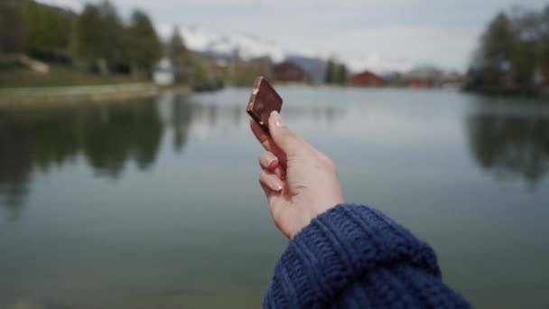Primer trozo de chocolate en mano femenina sobre fondo natural borroso — Vídeos de Stock
