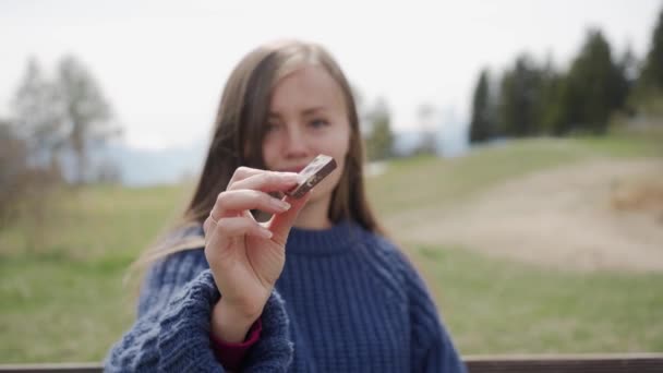 Vacker flicka i blå tröja håller en bit choklad i handen och smaka den utomhus i bergen. Att ha söt semester i Schweiz — Stockvideo