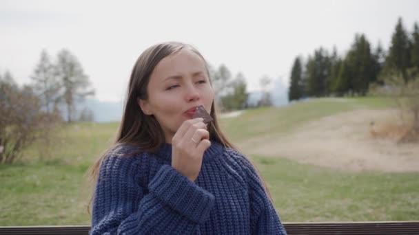 Menina bonita em suéter azul comendo pedaço de chocolate suíço saboroso nos Alpes — Vídeo de Stock