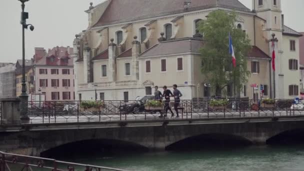 法国Annecy - 2019年5月8日：快乐的朋友一起健身训练或在雨天跑过桥。 在任何天气下都过着积极健康的生活 — 图库视频影像