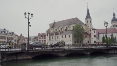 Sarı montlu ve şemsiyeli bir kız, Fransa 'nın yağmurlu havasında Annecy' de bir kanaldan köprünün karşısına yürür. Genel plan