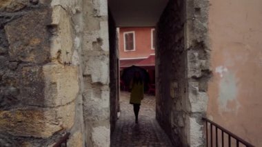 Sarı ceketli, şemsiyeli genç esmer kız Annecy Old Town, Fransa 'da dar kaldırımlı caddede yürüyor.
