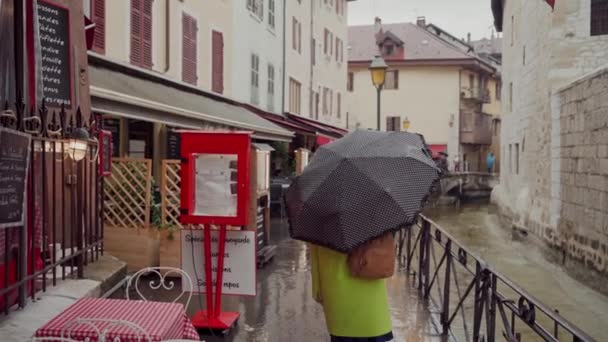 Mulher de casaco amarelo andar por ruas europeias velhas em clima chuvoso com guarda-chuva preto bolinhas — Vídeo de Stock