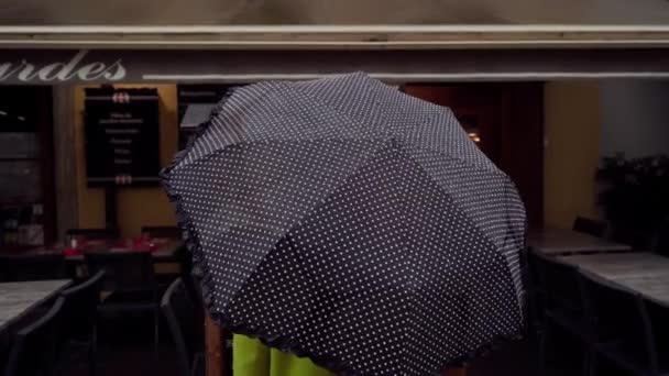 АННЕЦИЯ, ФРАНЦИЯ - 8 мая 2019 года: Человек с черным зонтиком в горошек читает меню возле уличного кафе и уходит. Вид сзади. Закрыть — стоковое видео