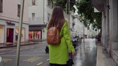 Annecy, Fransa - 8 Mayıs 2019: Sırt çantalı sarı ceketli bir kadın, yağmurdan sonra eski Paris şehrinde mobiletleriyle park alanının önünden geçiyor.
