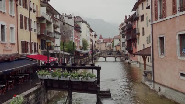 Vista del casco antiguo medieval francés de Annecy con fachadas de edificios coloridos, cafeterías turísticas, restaurantes y puente de piedra a través del río Thiou en días lluviosos — Vídeo de stock