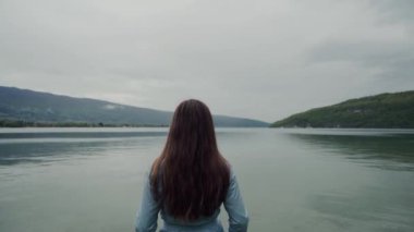 Rear view of long-hair brunette woman standing and enjoying scenic Alps and lake