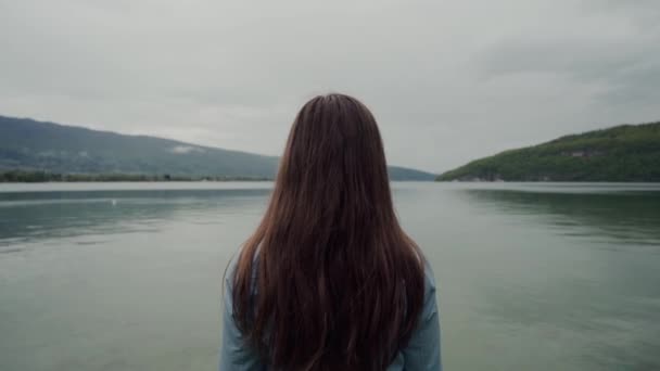 Visão traseira da morena de cabelos longos em pé e desfrutando de vistas panorâmicas das montanhas e do lago — Vídeo de Stock