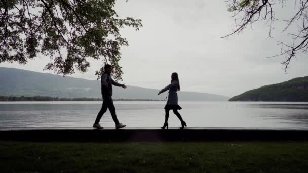 Młoda kochająca się para idzie do siebie z ramionami wyciągniętymi i przytulającymi się blisko jeziora pośród gór w deszczowy wiosenny dzień — Wideo stockowe
