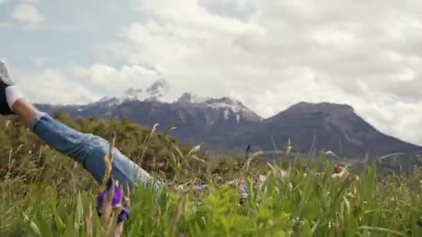 Happy woman lies down on an alpine meadow and gets up with smile. Camera rotation — ストック動画