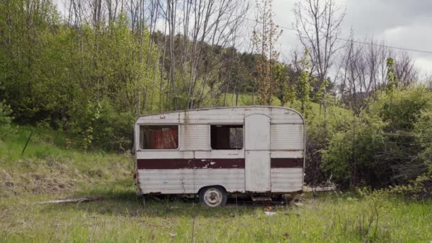 Frau kommt zu verlassenem Retro-Wohnwagen in wildes Gelände und setzt sich auf Bergkulisse — Stockvideo