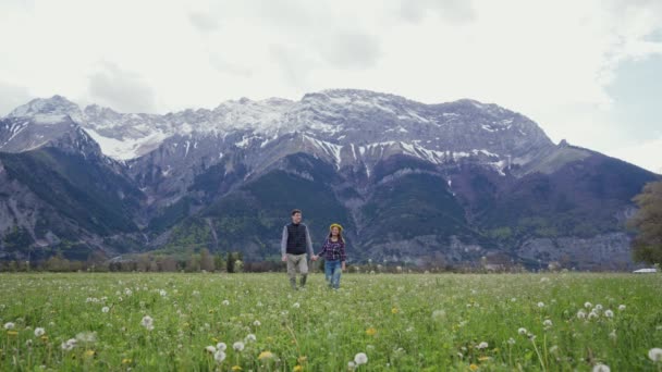 Щаслива жінка і чоловік йдуть по мальовничій гірській місцевості, тримаючись за руки. Активний відпочинок. Разом подорожуємо Альпами — стокове відео