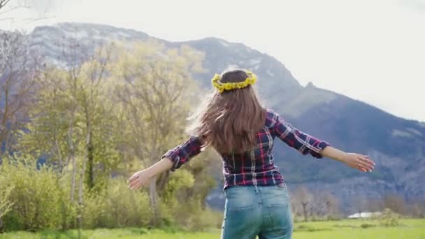 タンポポのリースを持つ美しい女性は笑顔で、山の風景の上に広げ腕で振り向く — ストック動画