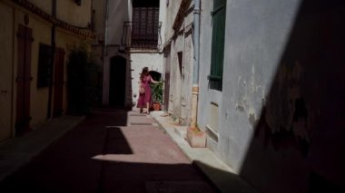 Kırmızı benekli elbiseli romantik kız eski şehrin dar sokaklarında yürüyor. Antibes 'teki Atmosferik Sokak. Fransa 'da tatil. Uzak plan