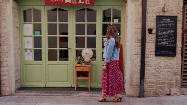 ANTIBE, FRANCE - 10 MAI 2019 : Jolie jeune femme en robe romantique à pois rouges marchant devant la vitrine du centre historique — Video