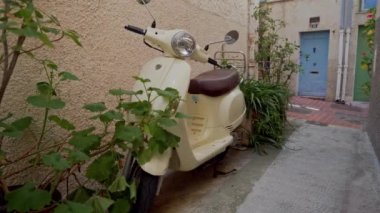 Antibes, Fransa 'da eski bir caddede çalılıklara park etmiş bej renkli scooter.