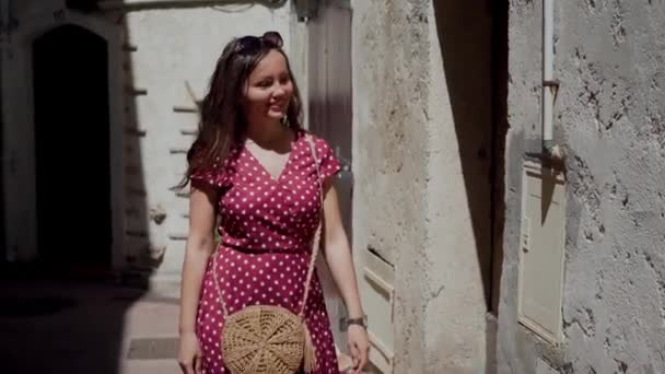 Piękna kobieta w czerwonej sukience w kropki spaceruje po starożytnej kamiennej ścianie starych budynków. Portret romantycznej zamyślonej dziewczyny — Wideo stockowe