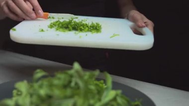 Kadın elleri kapalı bir kaseye yeşil salata dök, vejetaryen salatası hazırla.