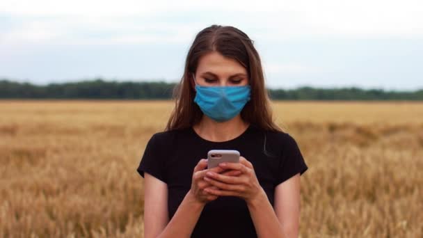 漂亮的年轻女子戴着医疗面罩 站在田野里看着电话 保护自己不受感染 — 图库视频影像