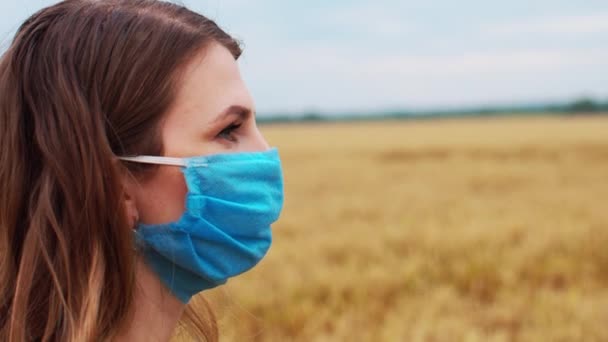 年轻姑娘戴着抗病毒口罩 凝视着田野 紧盯着摄像机 — 图库视频影像