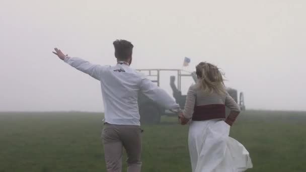 Kærlige unge par glædeligt kørende, bjerge tåge, bil i baggrunden. – Stock-video