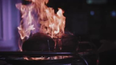 Şef bir restoranda et pişirir, alkol döker ve ateşe verir. Et tabakta döner.