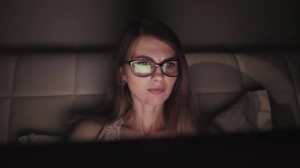 Houkutteleva nuori liikenainen työskentelee yöllä tietokoneen kautta toimistossa, lähikuva hipster-opiskelijatytöstä selaamassa Internetiä, katsomalla nykyaikaisen tietokoneen monitoria, keskittymällä laseihin — kuvapankkivalokuva