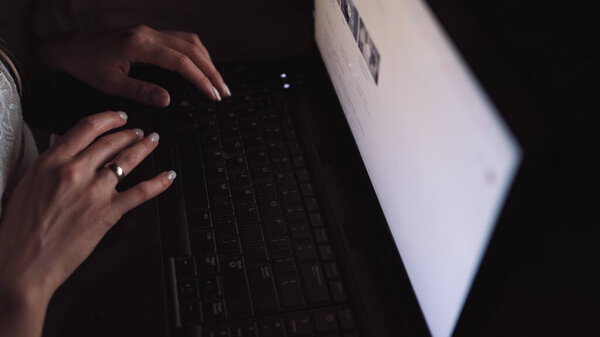 Girl looking for articles and photos on the Internet, in the dark under the blue light of the moon. Fingers working on the keyboard. Freelance work. Computer. Night. Writing an article, a letter