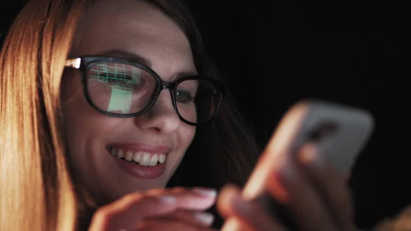 Beautiful young Woman Lying in Bed, Using Smart Phone and Smiling before Sleep. Woman using Cellphone on bed at Night. Attractive Girl looking at Mobile Phone.