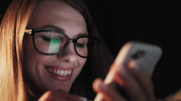 Vakker ung kvinne som ligger i sengen og bruker smarttelefon og smiler før hun sover. En kvinne som bruker mobiltelefon på senga. Attraktiv jente som ser på mobil. – stockfoto