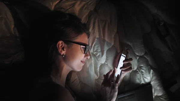Adolescente en pantalla táctil Smart Laptop y auriculares en la cama, estudiante en habitación oscura con luz nocturna móvil, una mujer joven estudiando y leyendo por la noche. — Foto de Stock
