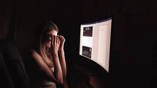 Nuori keskittynyt nainen, istuu huoneessaan tai toimistossaan.Opiskelee myöhään yöllä.Valvoo myöhään. Naisen tunne päänsärky ja kipu niskassa. — kuvapankkivalokuva