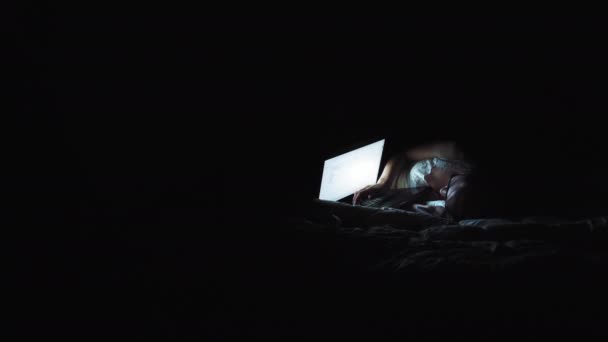 Buena chica viendo algo en un monitor portátil. Ambiente nocturno en el apartamento. La pantalla del ordenador portátil ilumina la cara de las niñas — Vídeos de Stock