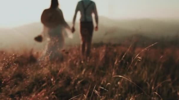 Jovem casal nas montanhas ao pôr do sol, em primeiro plano a grama — Vídeo de Stock