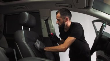 Arabanın içini kuru temizleme, bir adam lüks bir arabanın deri koltuğunun yanı sıra bir fırça ve mikrofiberle silmek için köpük uygular.