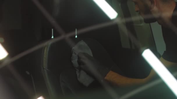 Автокресло моется в гараже, мужчина вытирает кожаное сиденье микроволокном, стреляя через стекло — стоковое видео