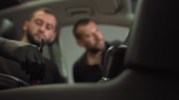 Lähikuva ammunta vaihteiston kahvat, kaksi työntekijää puhdistaa auton sisustus pölystä, etualalla käsi musta hansikas ja harja — kuvapankkivideo