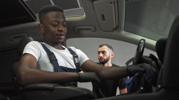 Afro-américain est venu au travail, aide à laver les intérieurs de voiture, jeune homme joyeux aide à nettoyer l'intérieur de la voiture, deux travailleurs au travail dans le garage — Video