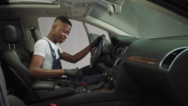 Un joven afroamericano limpia el coche, trabaja en el lavado de autos, un adolescente alegre gana después de entrenar en el lavado de autos — Vídeo de stock